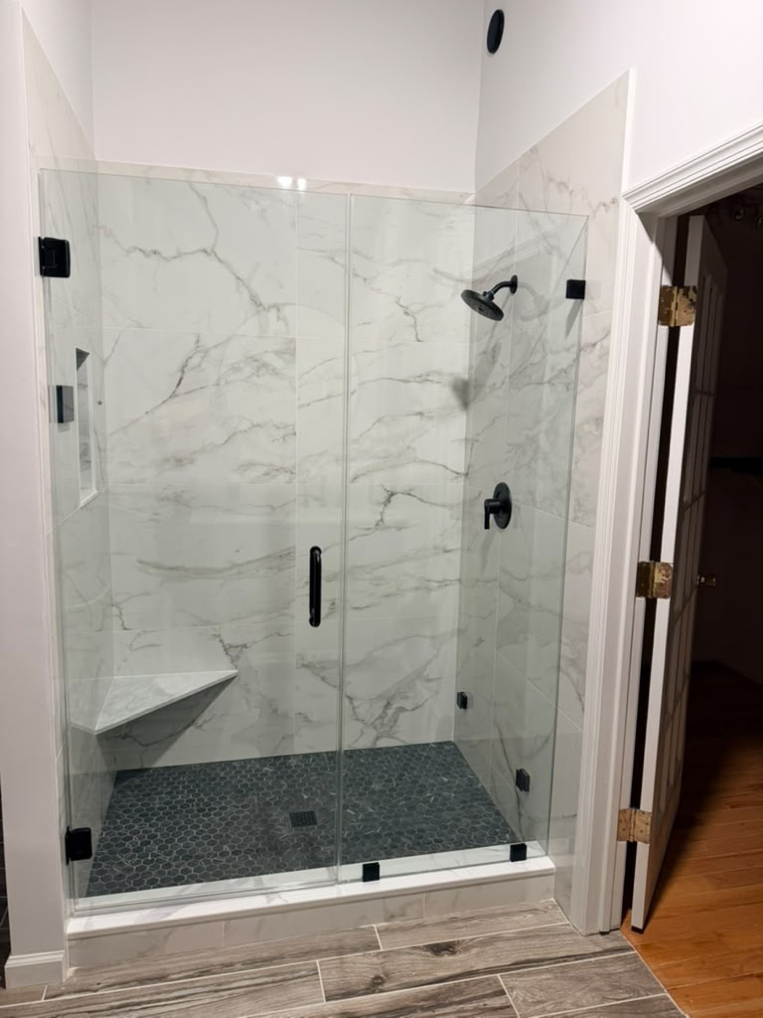 After: frameless shower door and panel with matte black hardware on marble tile