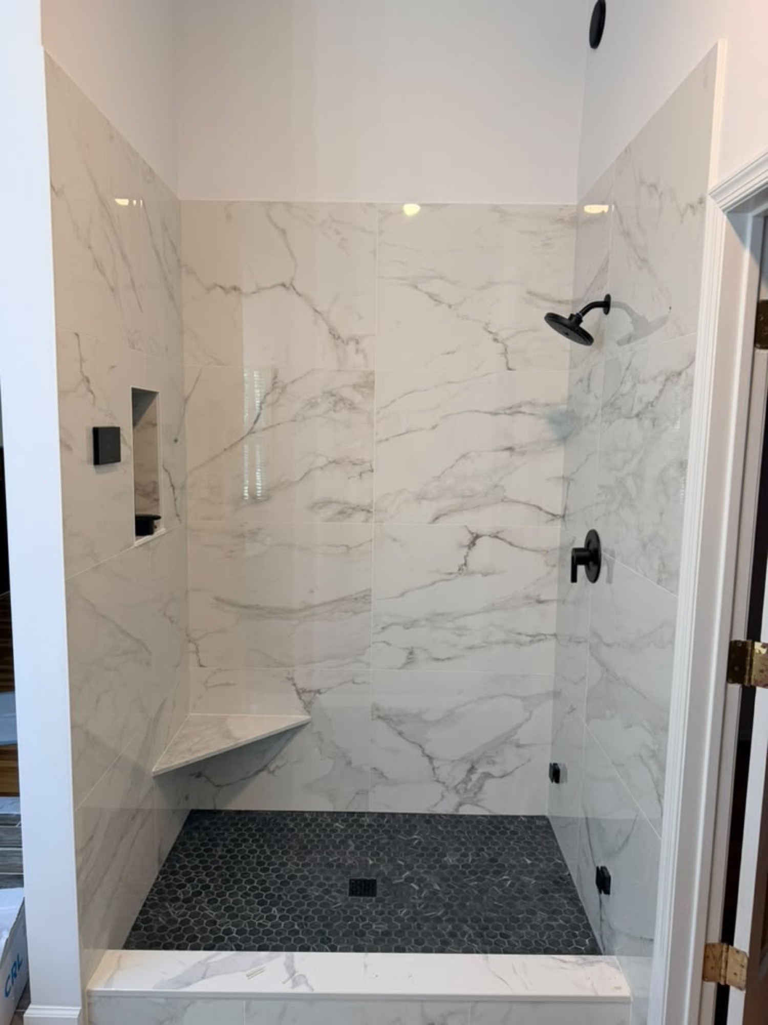 Before: marble tile shower with matte black fixtures, no glass installed