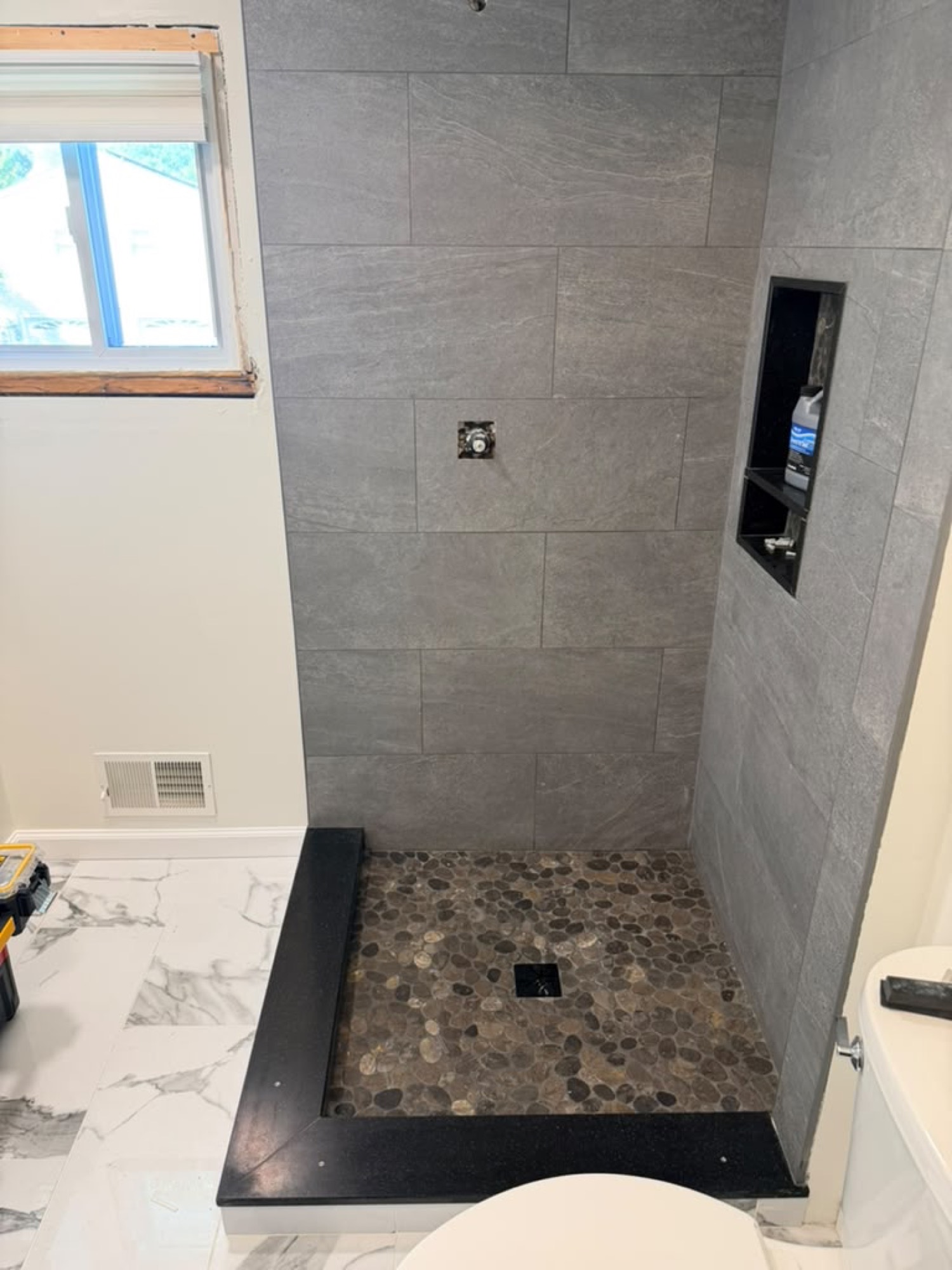Before: gray tile shower with pebble floor, no glass installed
