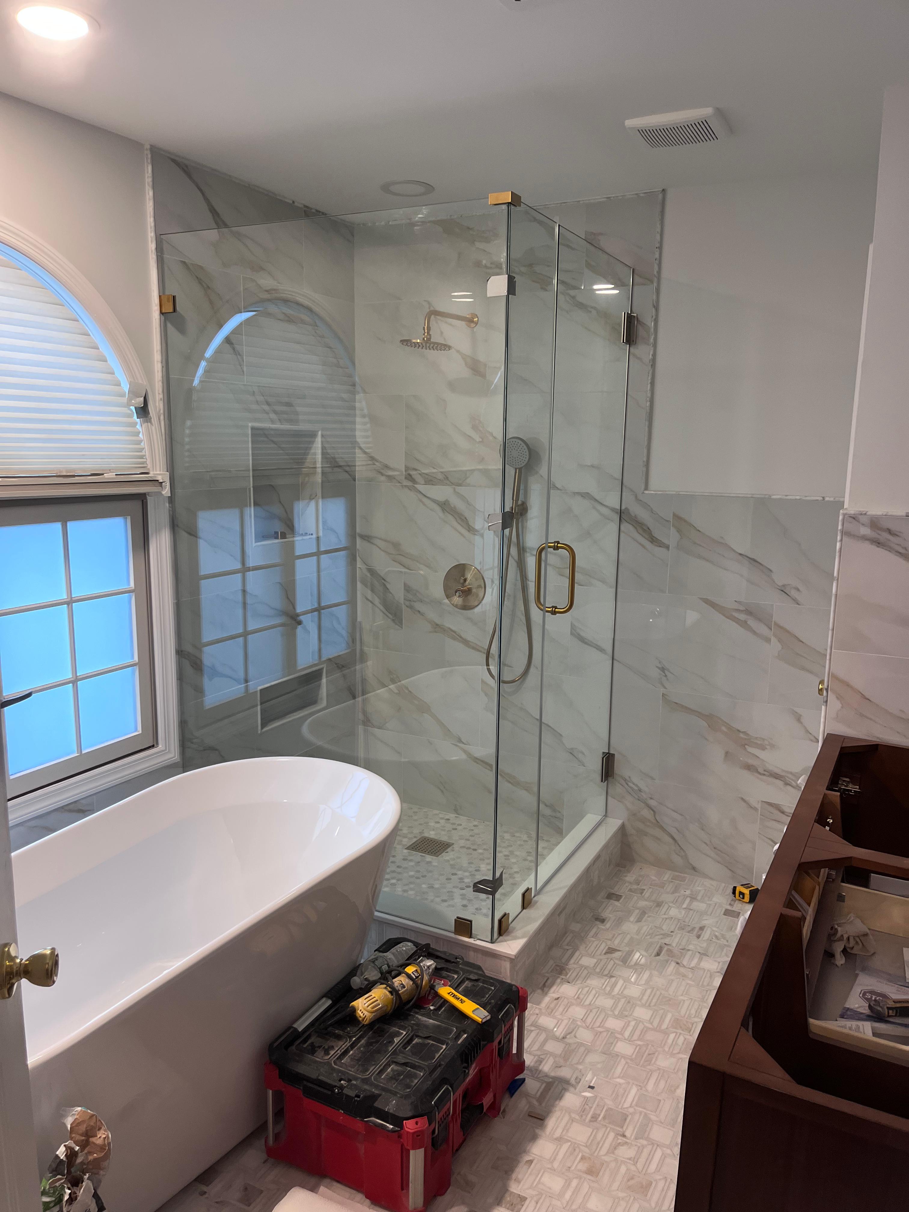 Walk-in frameless shower with notch panel and brushed gold hardware on white marble
