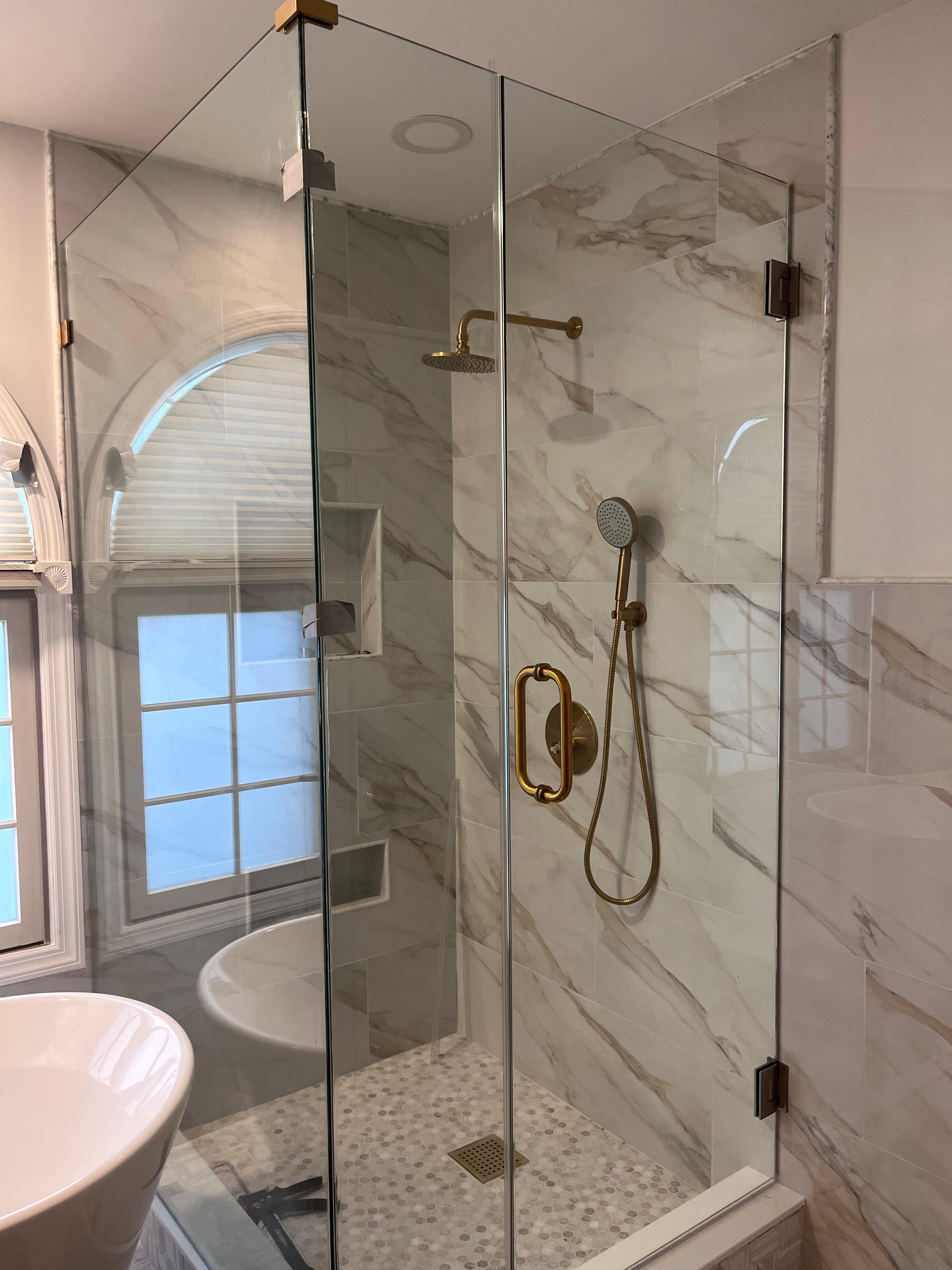 Frameless shower door with brushed gold hardware and travertine tile surround