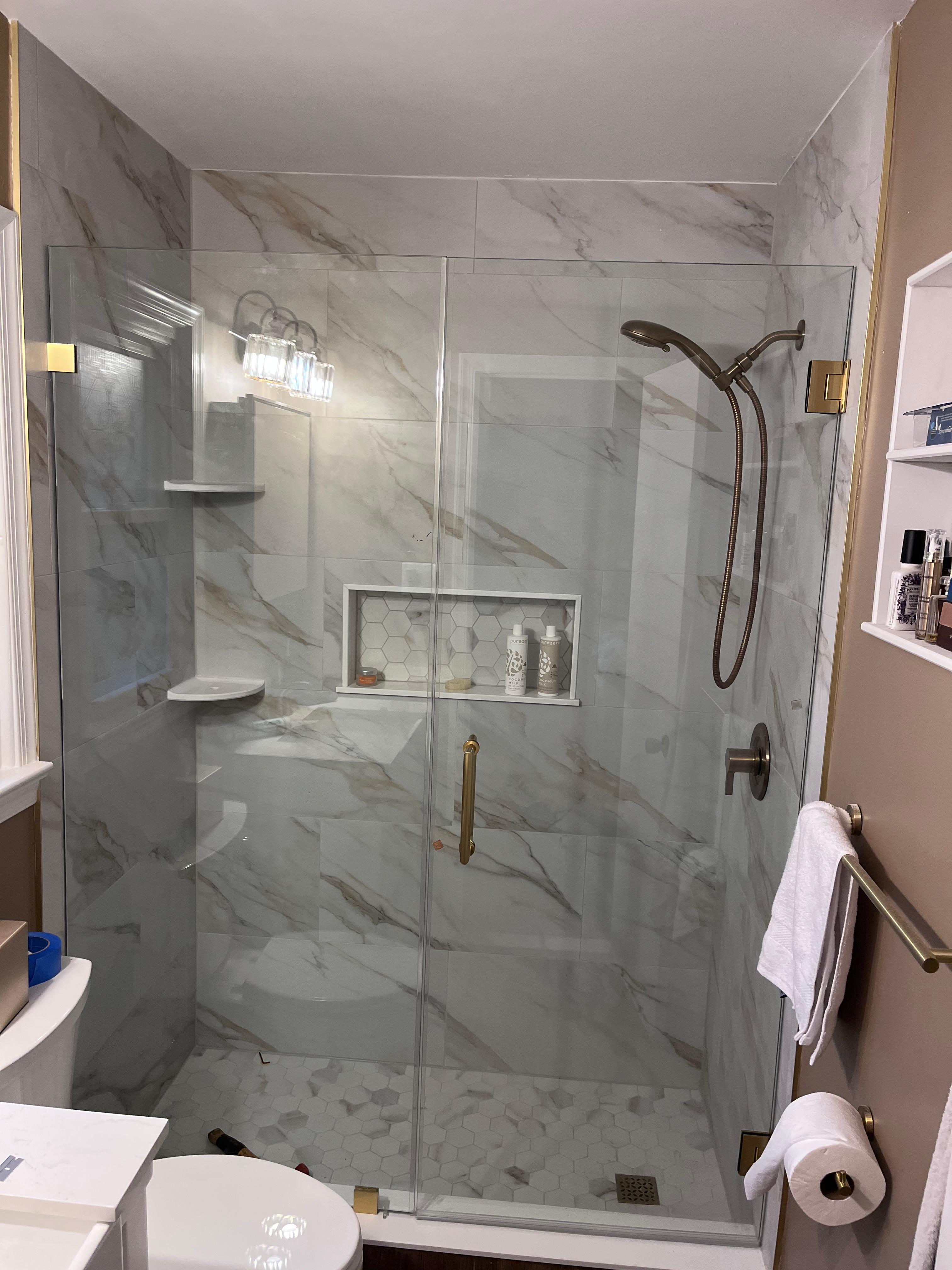 Frameless shower door with brushed gold hardware on white marble with built-in niche