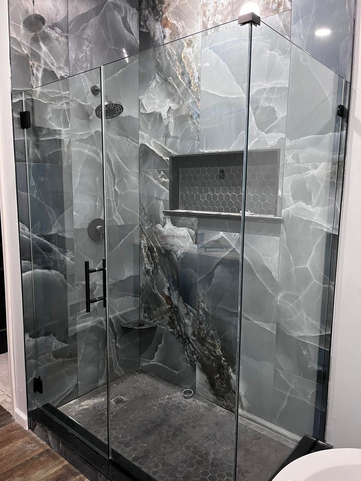 Close-up detail of frameless shower door with matte black hardware on Calacatta marble