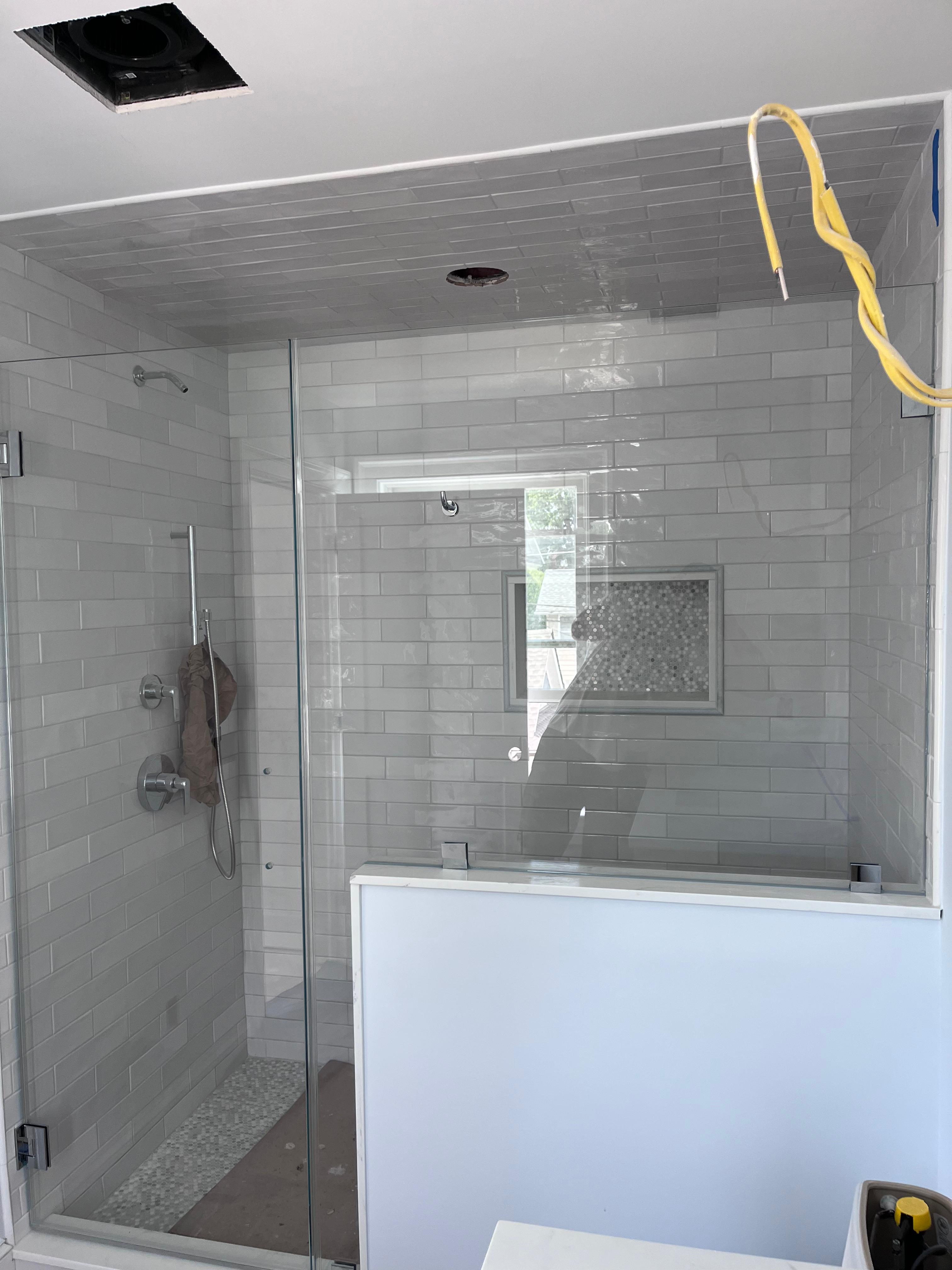 Frameless shower door and notch panel with brushed nickel hardware on white subway tile