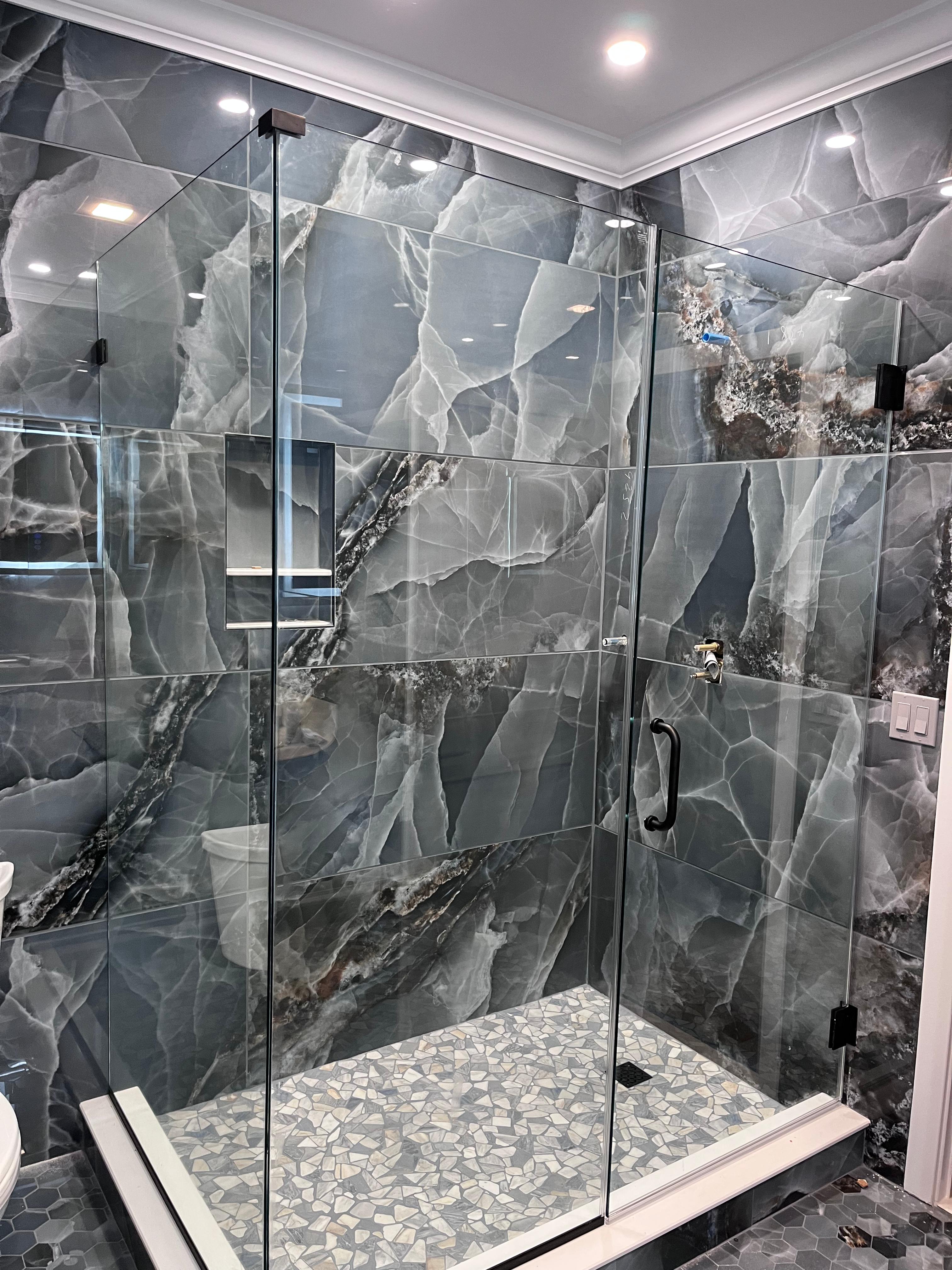 Frameless shower enclosure with matte black hardware on dark marble