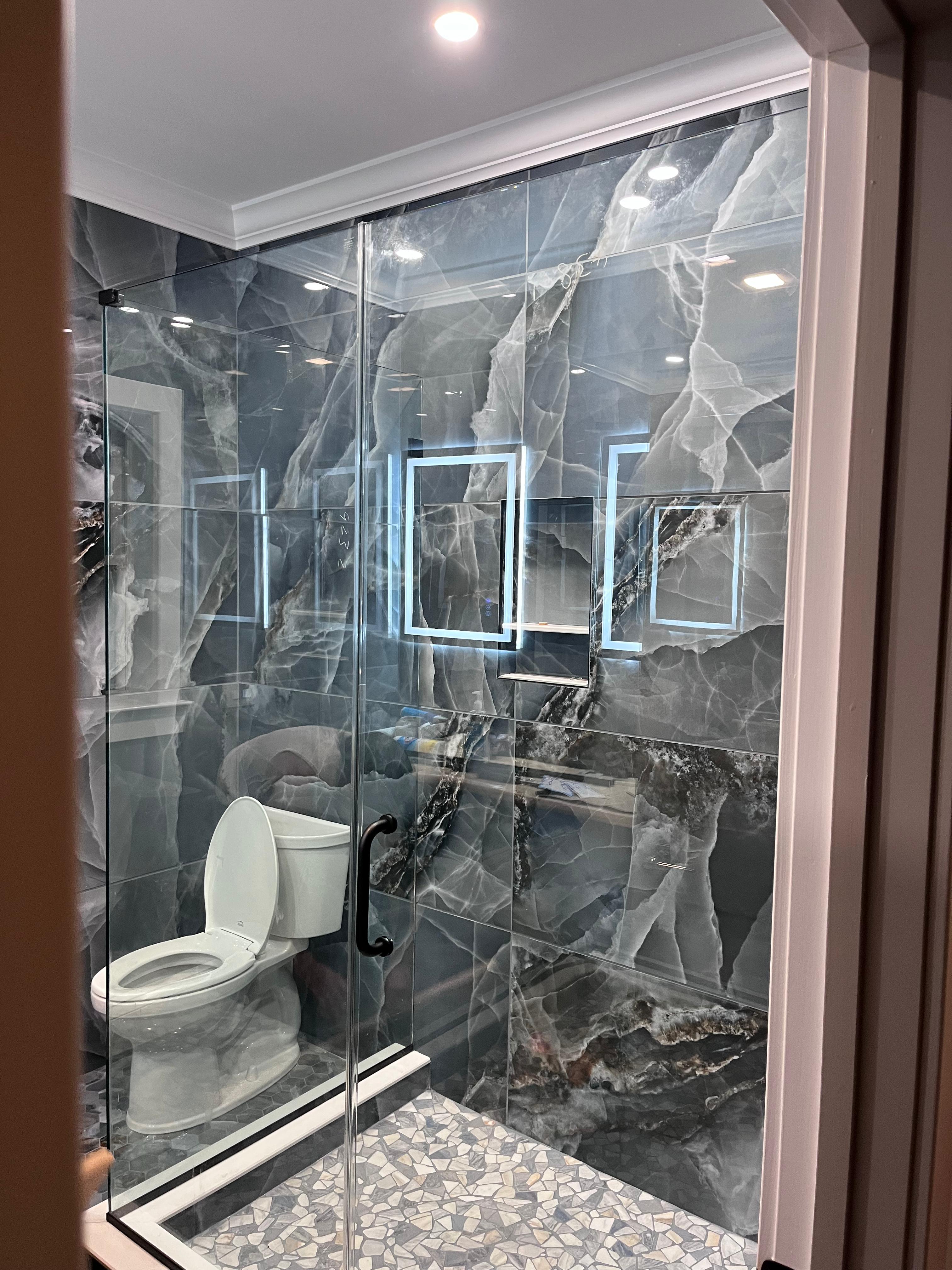 Frameless sliding bypass shower door with matte black hardware on dark marble tile