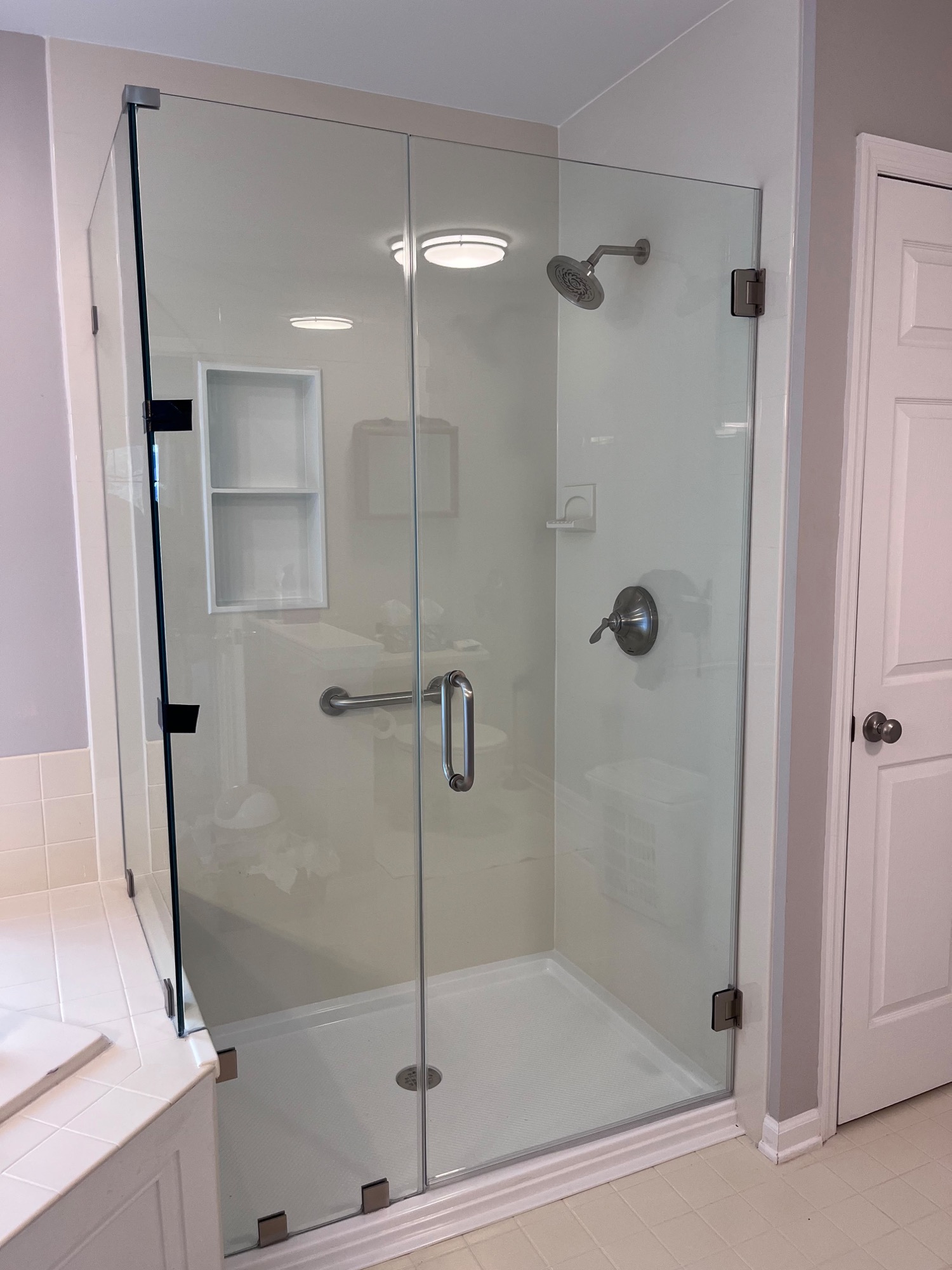 Frameless shower door with brushed gold hardware and gold-trimmed niche on marble tile