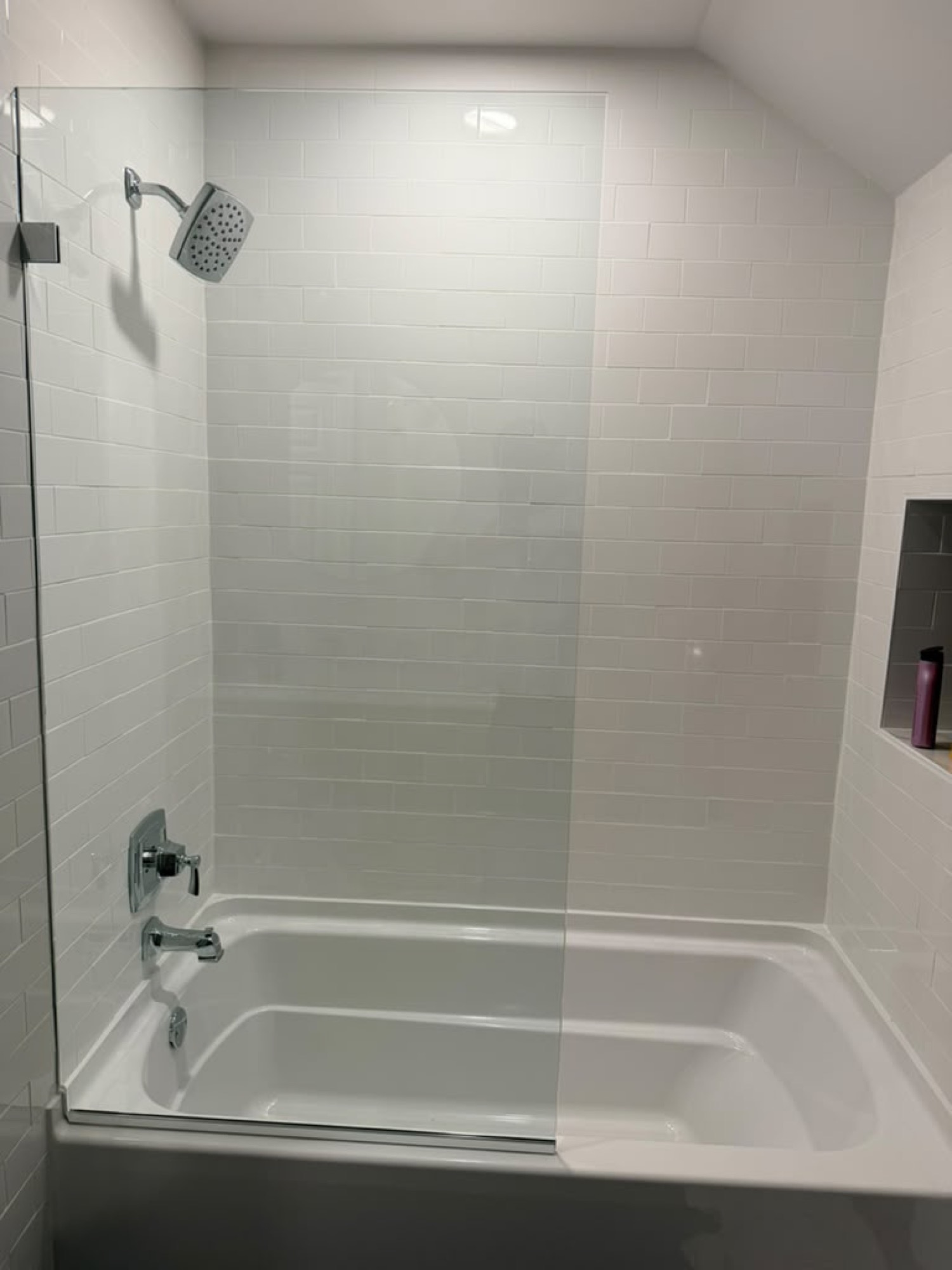 Bathtub with a fixed glass splash panel and chrome hardware on white subway tile
